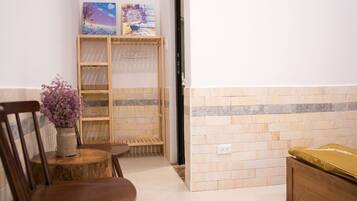 Un pasillo con una silla de madera, una mesita con un florero y un armario de madera, además de un estante en la pared con obras de arte.