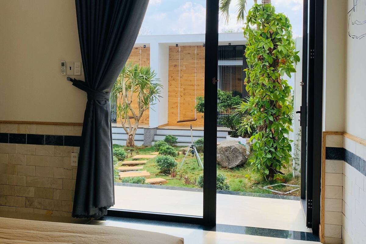 Un dormitorio con cama, puerta corrediza de vidrio que da a un jardín con plantas y una estructura de madera.