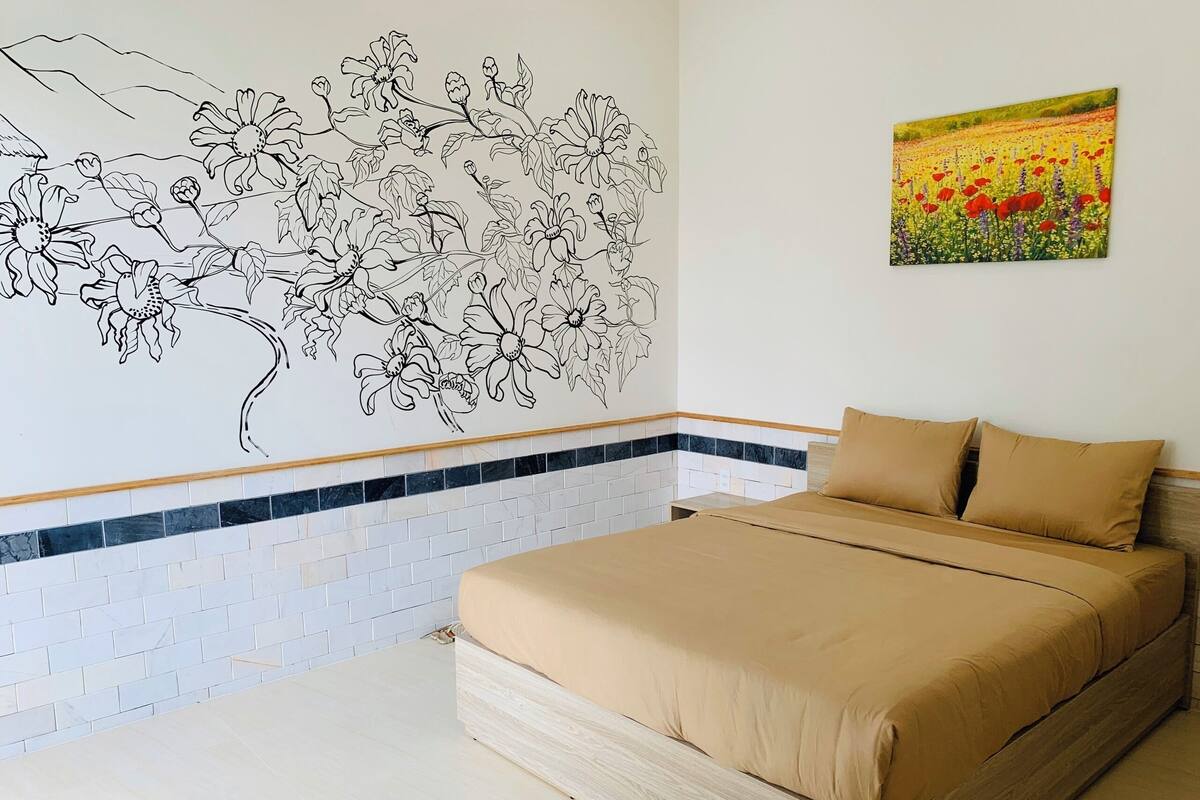 Un dormitorio con cama, un mural floral, piso de baldosas y un cuadro de un campo.