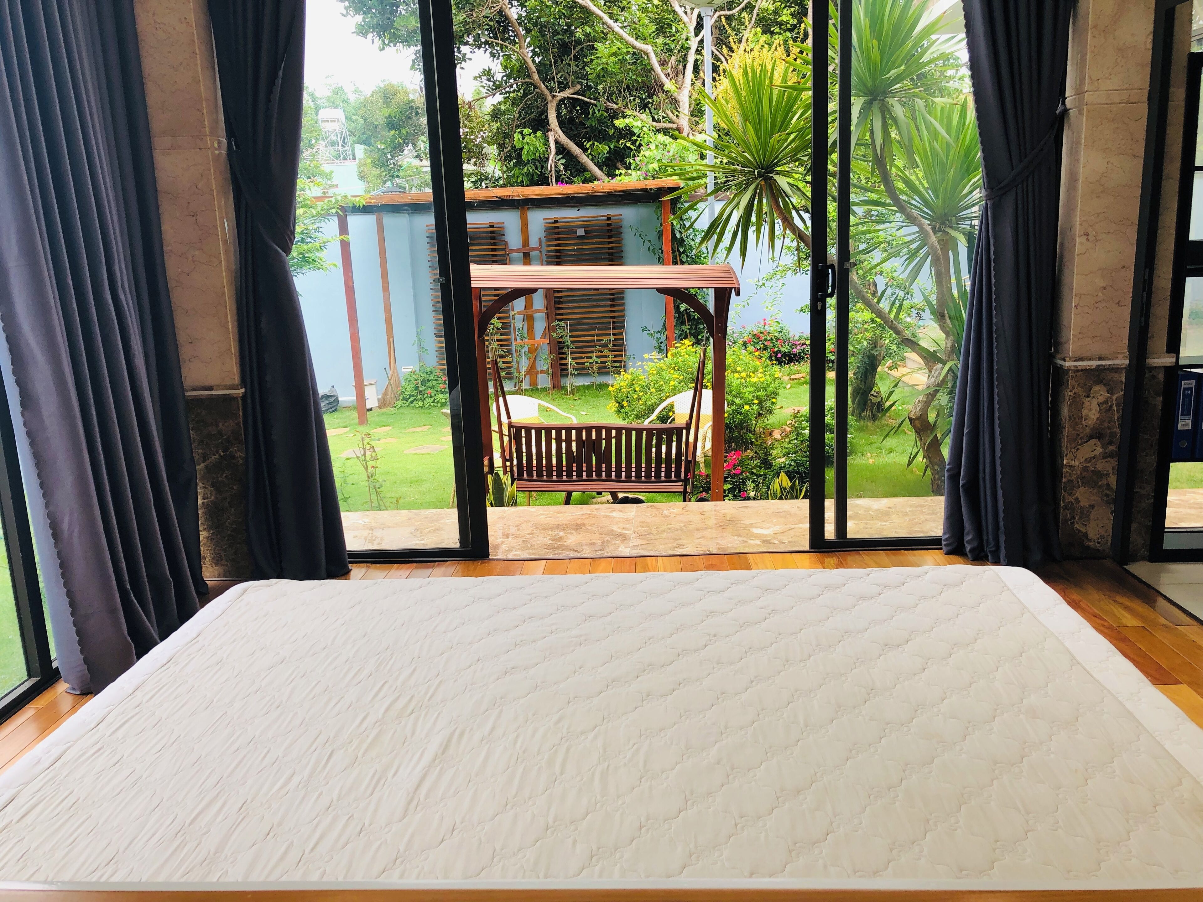 Una habitación con un ventanal grande, una cama y vistas a un jardín con una estructura de madera y plantas.