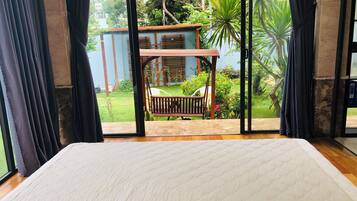 Una habitación con un ventanal grande, una cama y vistas a un jardín con una estructura de madera y plantas.