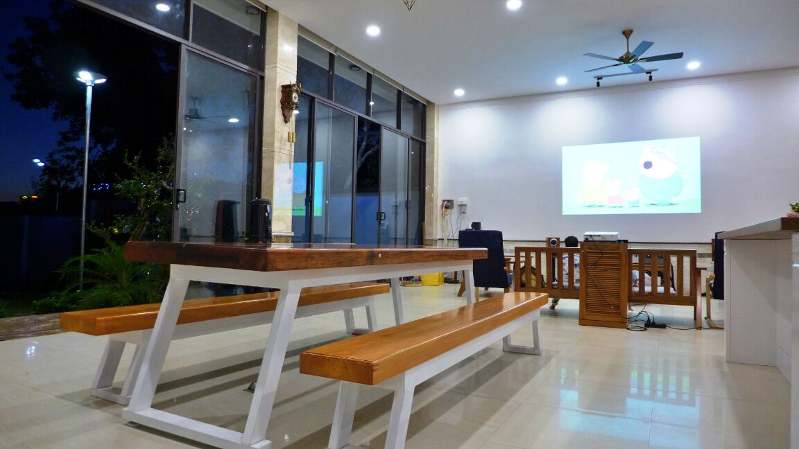 Un espacio interior moderno con un banco de madera, una pantalla de proyector y un ventilador de techo.