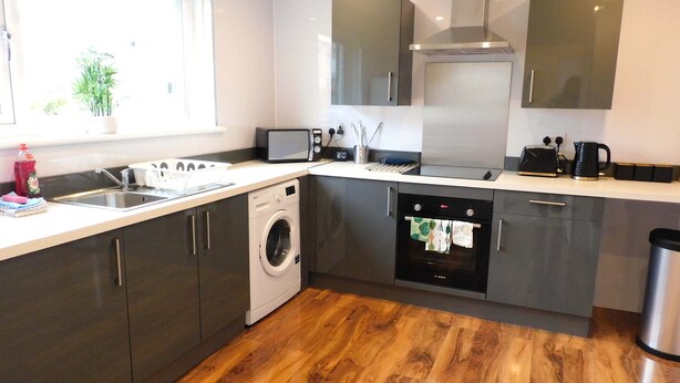 A modern kitchen with a washing machine, oven, microwave, and stainless steel appliances. - 4 Bedroom, Newly Refurbished Home in East Kilbride (East Kilbride)