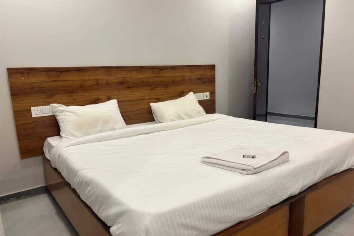 A neatly made bed with white linens and pillows, a wooden headboard, and a grey door in the background.