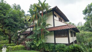 A two-story house with a tiled roof, surrounded by lush greenery and a small staircase leading to the entrance. - Nongsa Village (Batam)