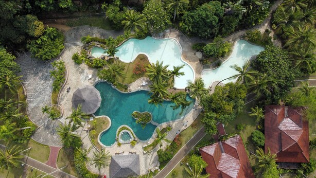 An aerial view of a resort with multiple swimming pools surrounded by lush greenery and palm trees. - Nongsa Village (Batam)