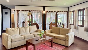 A living room with two beige sofas, a wooden coffee table, and a ceiling fan. - Nongsa Village (Batam)