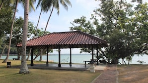 A covered pavilion with a tiled roof, surrounded by palm trees and a view of the water. - Nongsa Village (Batam)
