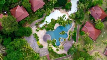 Luchtbeeld van een resort met meerdere gebouwen met rode daken, een centraal gelegen zwembad en omliggend weelderig groen.