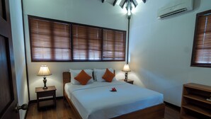 A neatly made bed with white linens and orange pillows, two bedside lamps, and a wooden headboard. - Nongsa Village (Batam)