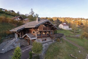 A wooden cabin with a stone foundation, a wooden deck, and a view of a hillside.