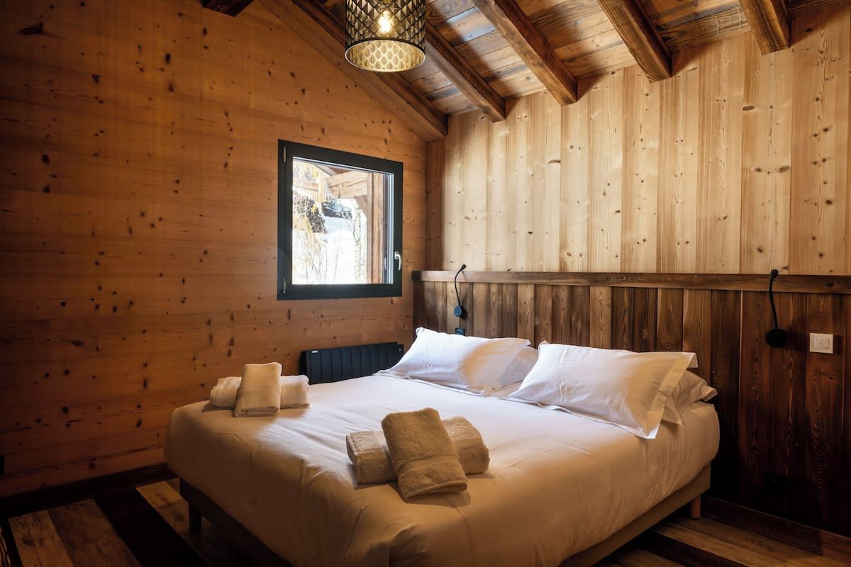 A wooden room with a bed, pillows, and towels.