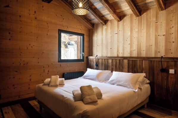 A wooden room with a bed, pillows, and towels.