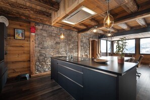 Una cocina moderna con una isla grande, pared de piedra, techo de madera y ventanas amplias.