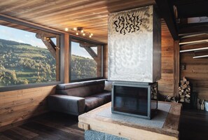 A modern interior with a wooden ceiling, a large window offering a view of a green landscape, a built-in fireplace, and a seating area.