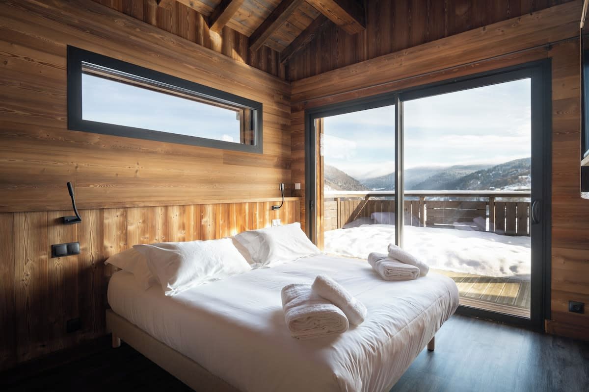 A wooden cabin bedroom with a large bed, a window, and a view of a snowy landscape.