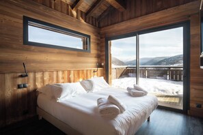 A wooden cabin bedroom with a large bed, a window, and a view of a snowy landscape.