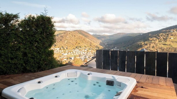 Un bain à remous sur une terrasse en bois, avec vue sur une ville et des collines en arrière-plan.