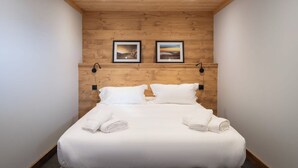 Une chambre d’hôtel avec un plafond en bois, deux tableaux encadrés au mur, un lit avec du linge de maison blanc et deux lampes fixées au mur.