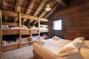 A wooden cabin room with bunk beds, a large bed, and a window.