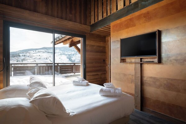 A hotel room with a bed, a TV mounted on the wall, and a large window offering a view of a snowy landscape.