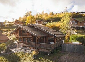A wooden cabin with a balcony, surrounded by a hilly landscape.