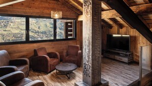 Une pièce chaleureuse avec un décor intérieur en bois, une grande fenêtre, un téléviseur et une cheminée.
