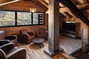Una habitación acogedora con detalles de madera, un ventanal grande, televisor y chimenea.