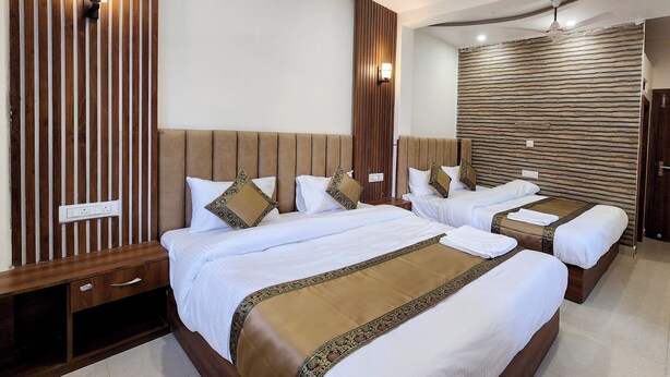 Habitación de hotel con tres camas, paneles de madera e iluminación en la pared.