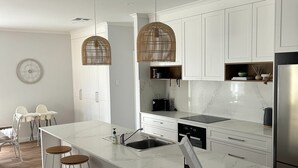 Een moderne keuken met witte kasten, een groot eiland met krukken, hanglampen en een roestvrijstalen koelkast.