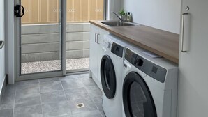 Een kleine wasruimte met een wasmachine, een wastafel en een schuifdeur naar een balkon.