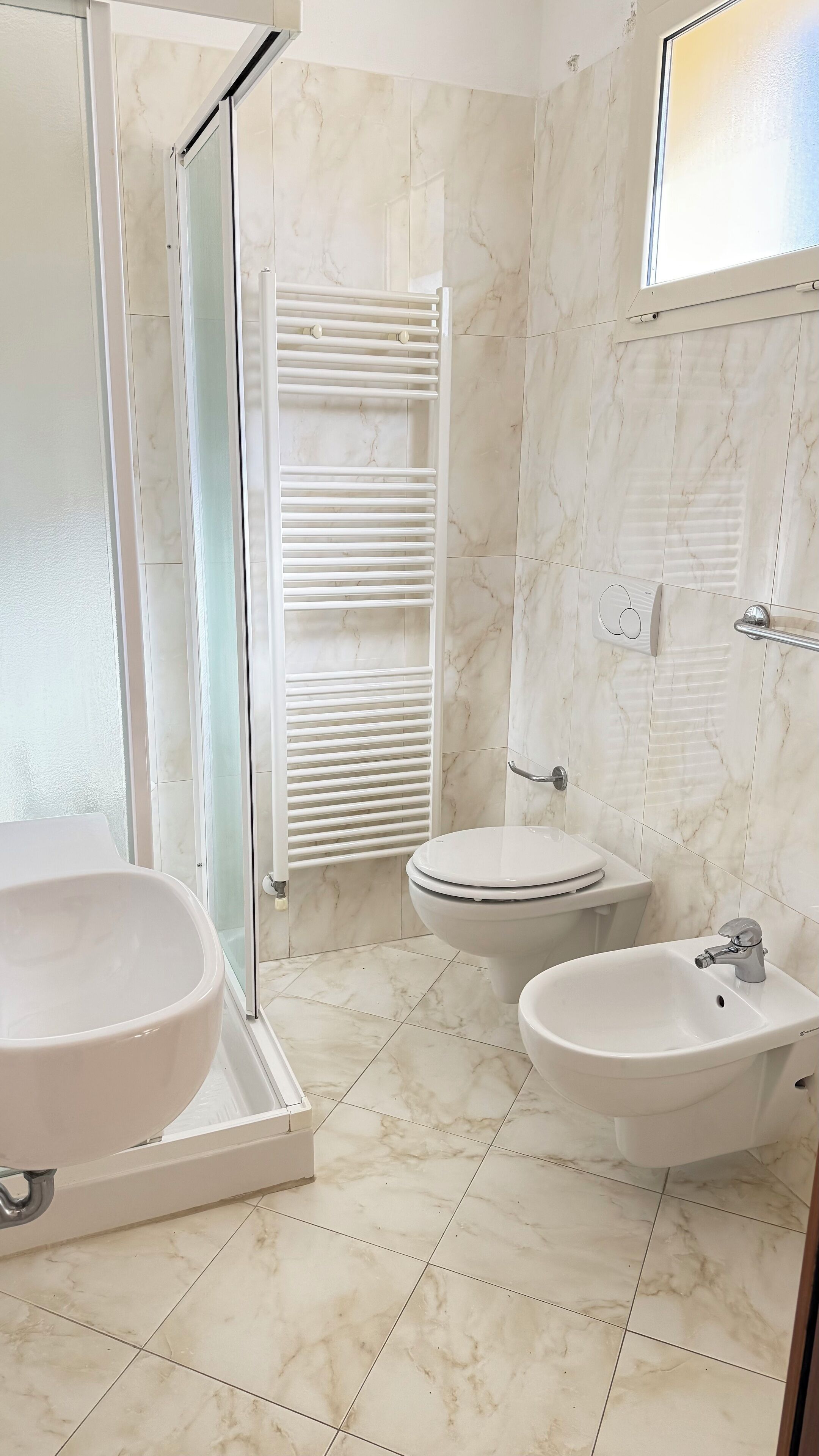A bathroom with a shower, toilet, bidet, and sink.