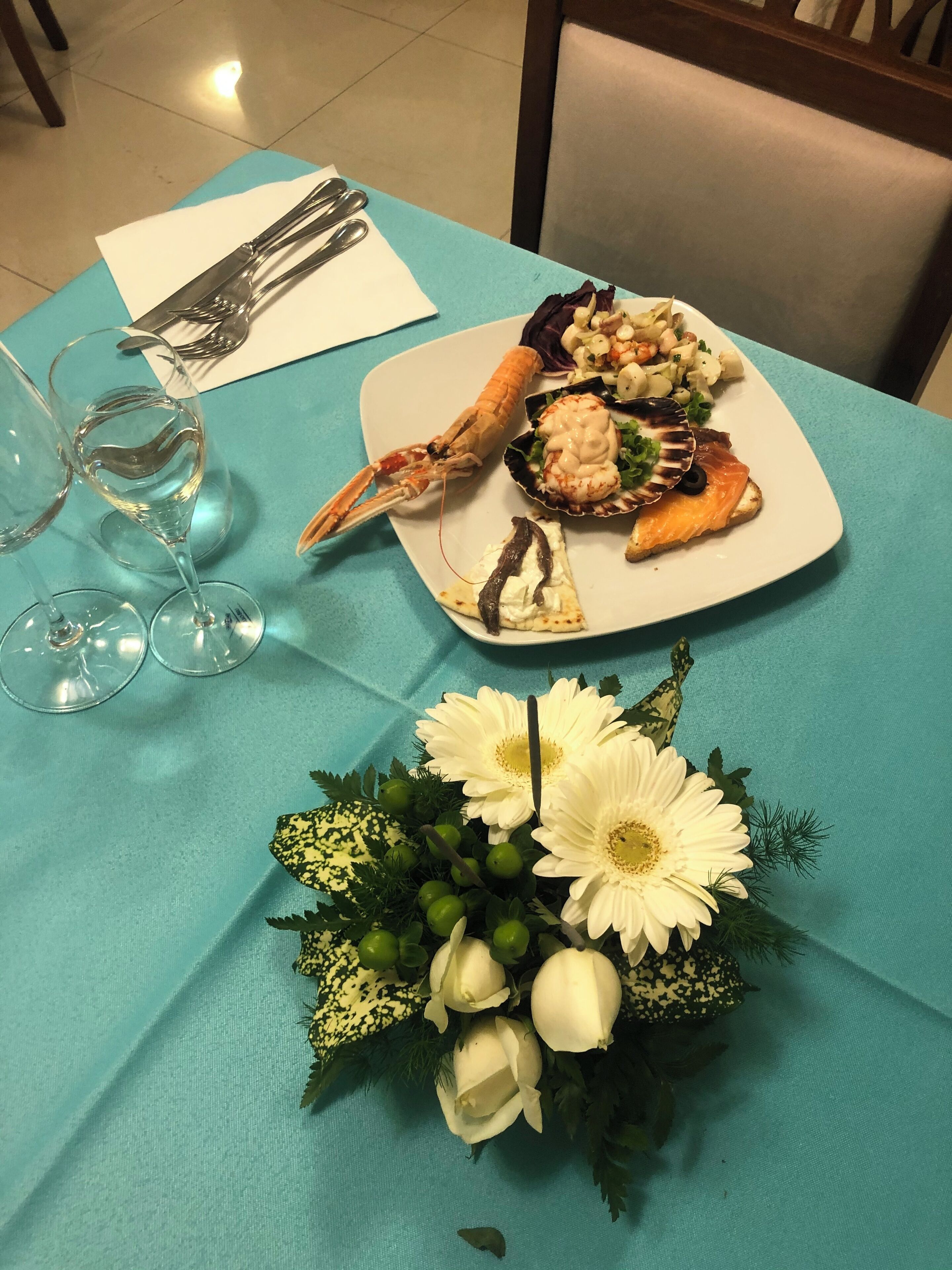 Ett bord dukat med ett fat med skaldjur, vinglas och en blomsterdekoration i mitten.