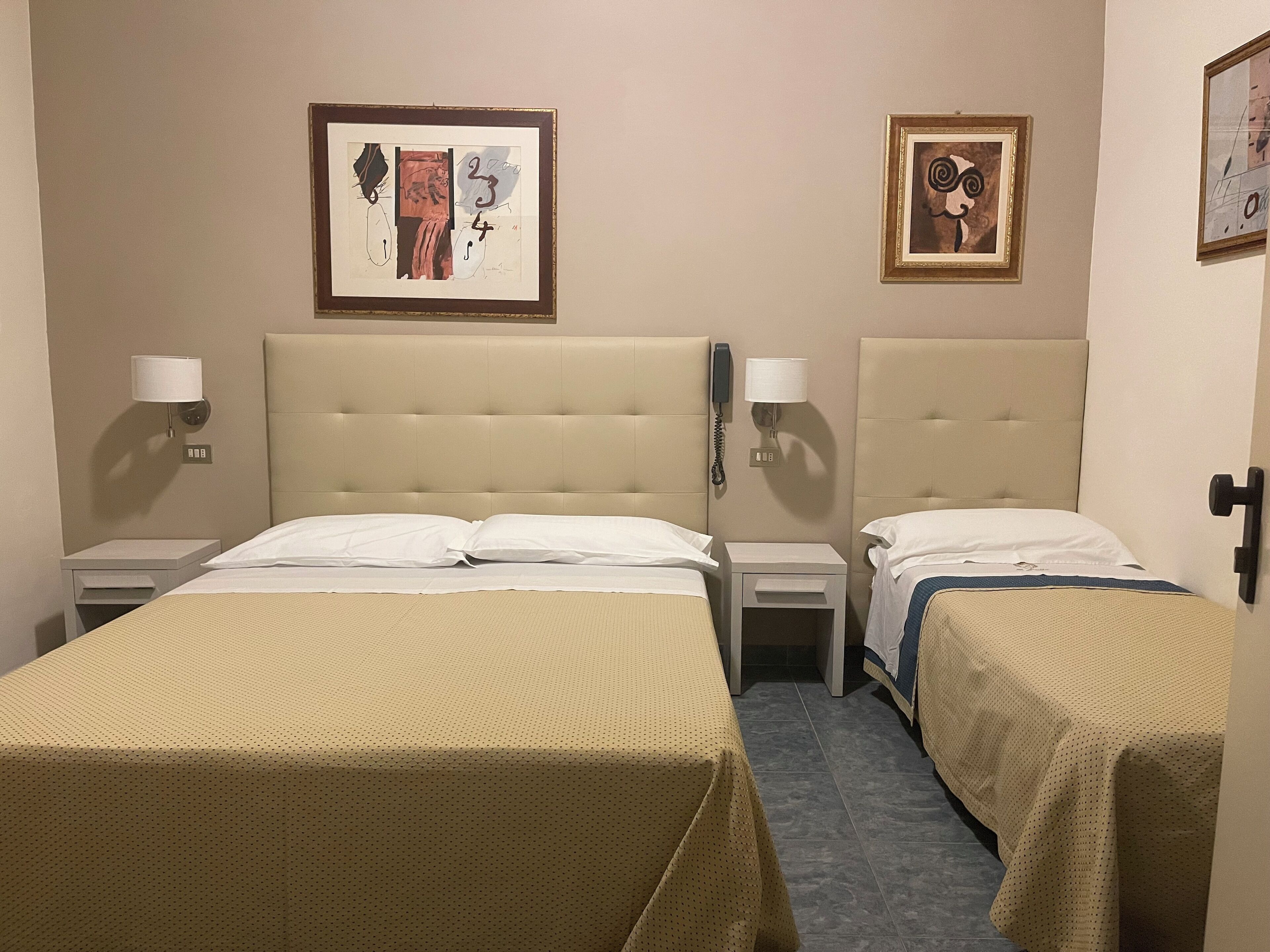 A hotel room with two beds, each with a headboard, bedside tables, lamps, and framed artwork on the walls.
