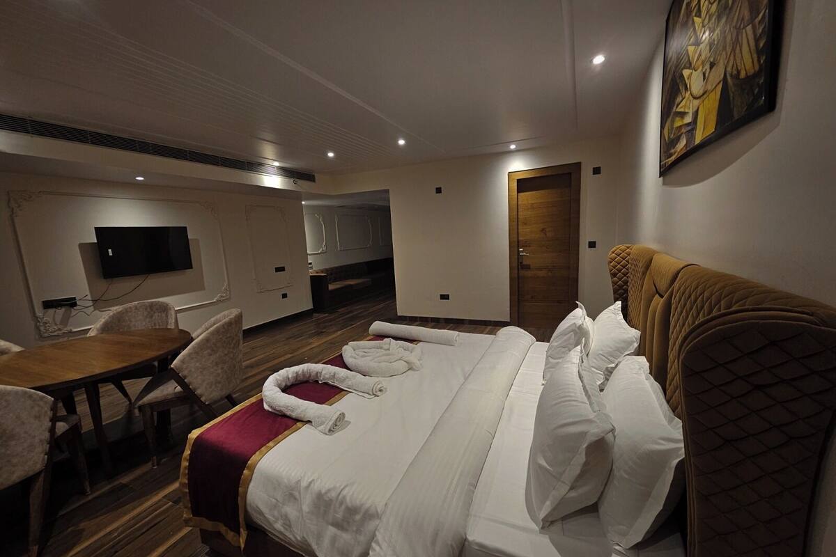 A hotel room with a bed, a desk, a chair, a TV, and a door.