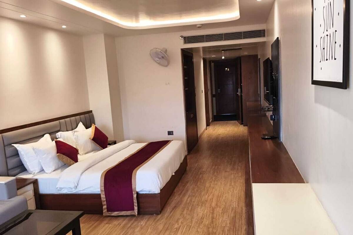 A hotel room with a bed, bedside table, and a hallway leading to a door.