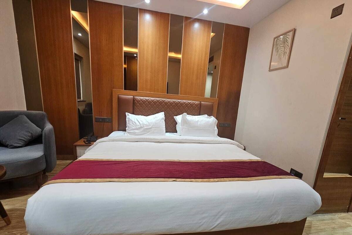 A hotel room with a large bed, a wooden headboard, a grey armchair, and a wooden wardrobe.