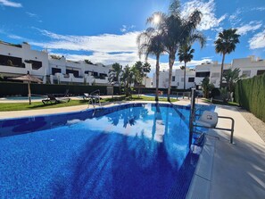 A swimming pool with lounge chairs and palm trees, surrounded by white buildings. - Cozy Beachside Haven (Pulpi)