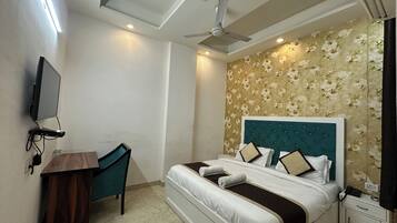 A bedroom with a bed, a desk, a television, and a ceiling fan.