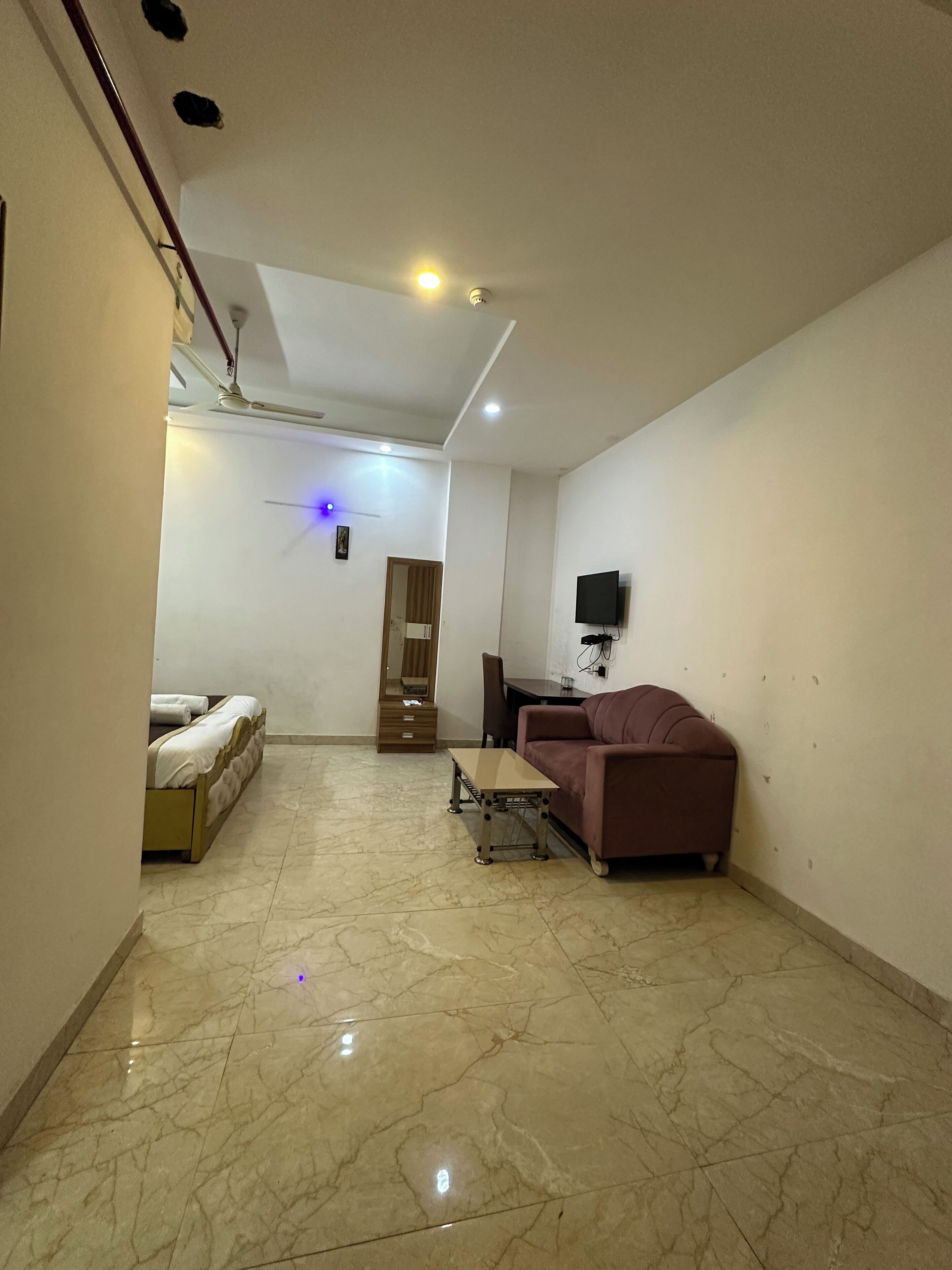 Une chambre d’hôtel avec un lit, une petite table, un canapé, une télévision et un ventilateur de plafond.