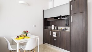 Een compacte keuken met donker houten kastjes, een wit aanrechtblad en een kleine eethoek met witte stoelen.