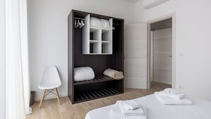 Een moderne slaapkamer met een grote kast, een bed met keurig opgevouwen handdoeken, en een stoel.