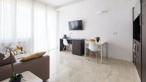 Een moderne woonkamer met een bank, een eettafel met stoelen, een aan de muur bevestigde televisie en een keuken met kasten.