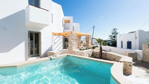 A modern white building with a swimming pool, stone pillars, and a wooden pergola. - Triotissa Local Living Residences (Paros)