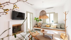 A modern living room with a fireplace, a sofa, a coffee table, and a hanging light fixture. - Triotissa Local Living Residences (Paros)