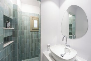 Ein Badezimmer mit einem weißen Waschbecken, einem runden Spiegel und grünen Fliesen.