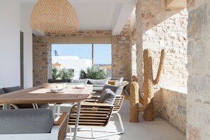 Un área de comedor exterior moderna con pared de piedra, mobiliario de madera y una lámpara tejida.