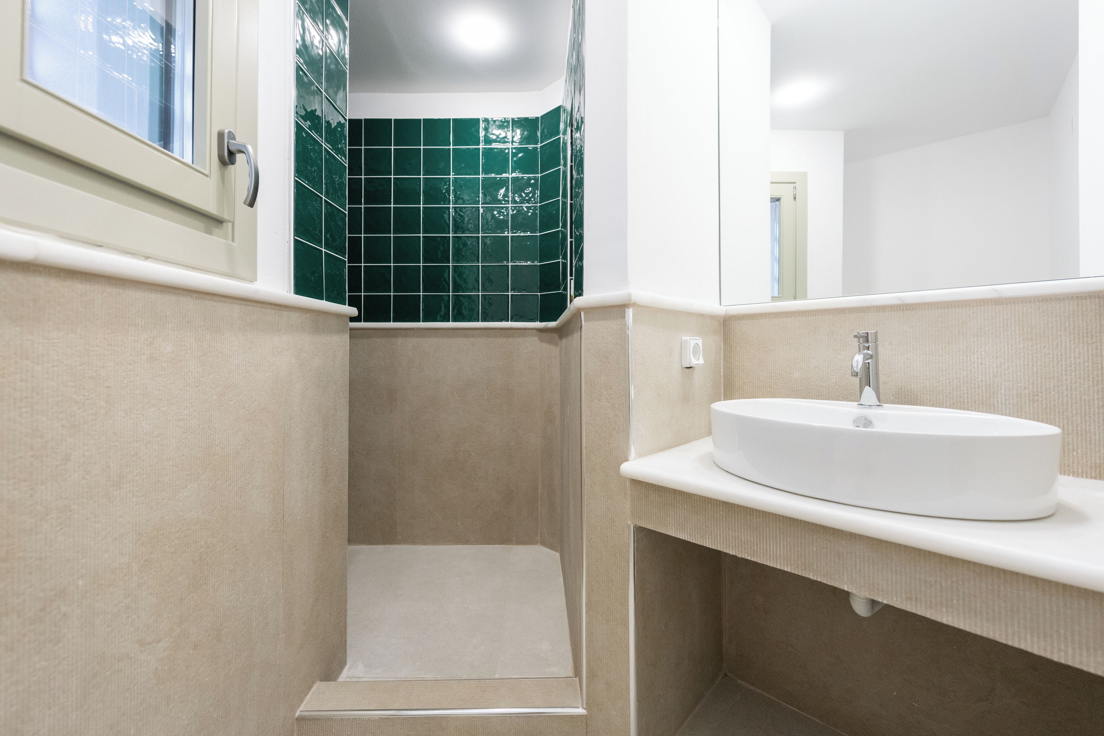 Une salle de bain avec un lavabo blanc, des murs de couleur beige et une zone de douche carrelée de carreaux verts.