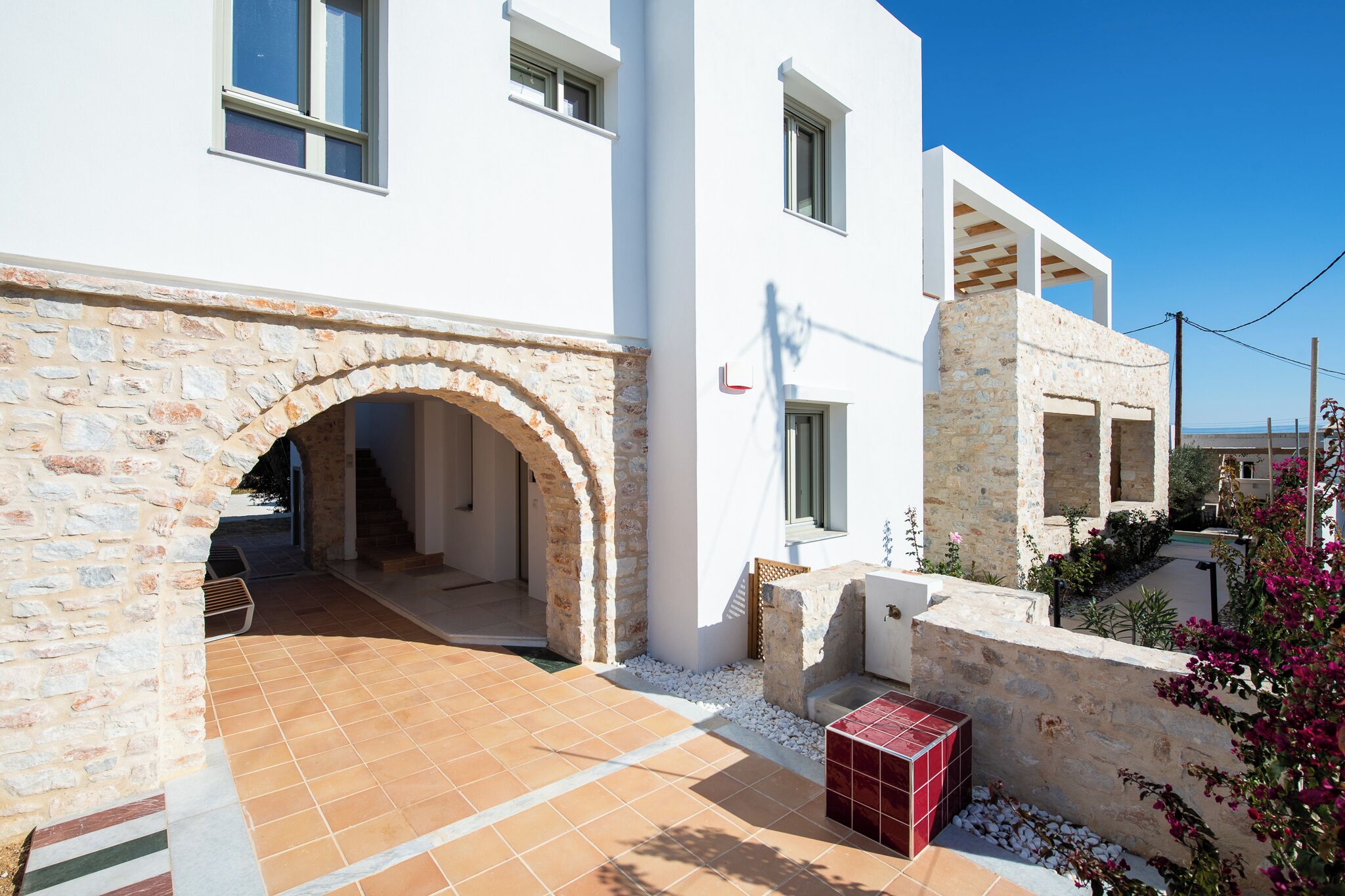A modern building with a stone archway entrance, a tiled patio, and a small garden area with flowers.