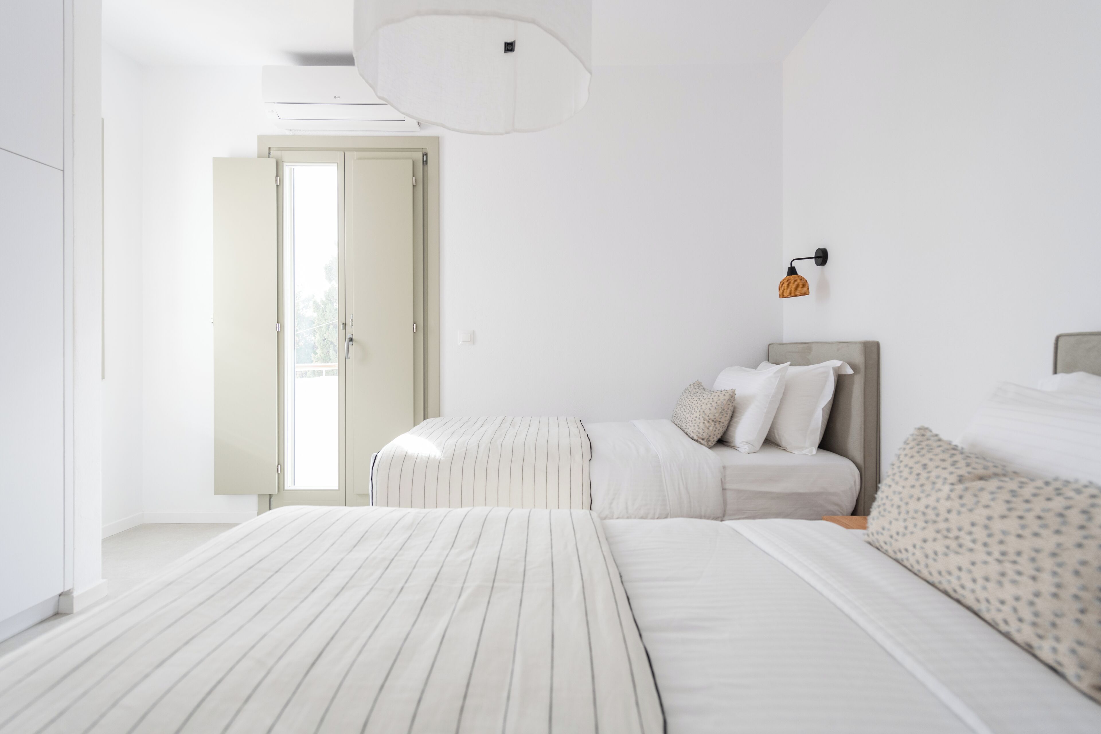 A minimalist bedroom with two beds, a large window, and a ceiling light fixture.